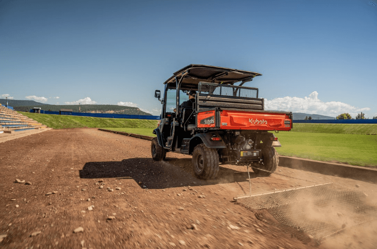 The rear shot of a Kubota utility vehicle driving down a dirt road