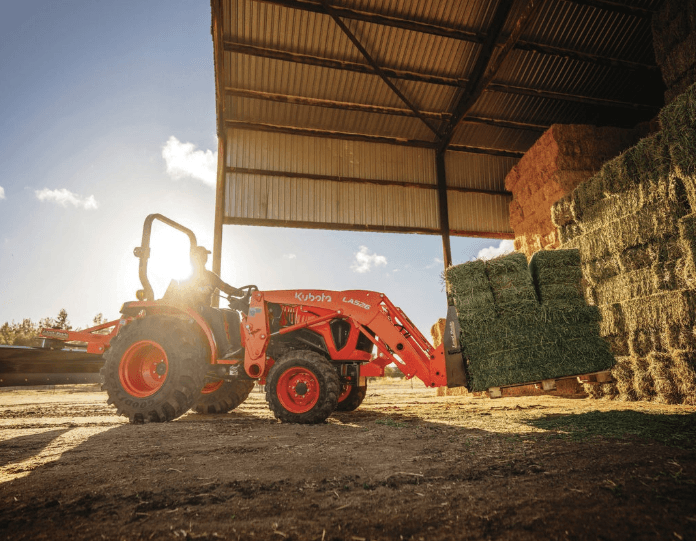 A Kubota L3902 Tractor lifting a pallet of hay stacks